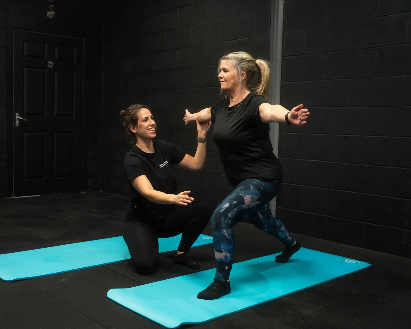 A MotionWorks physiotherapist guiding a client through a lunge on a turquoise mat in the training studio.