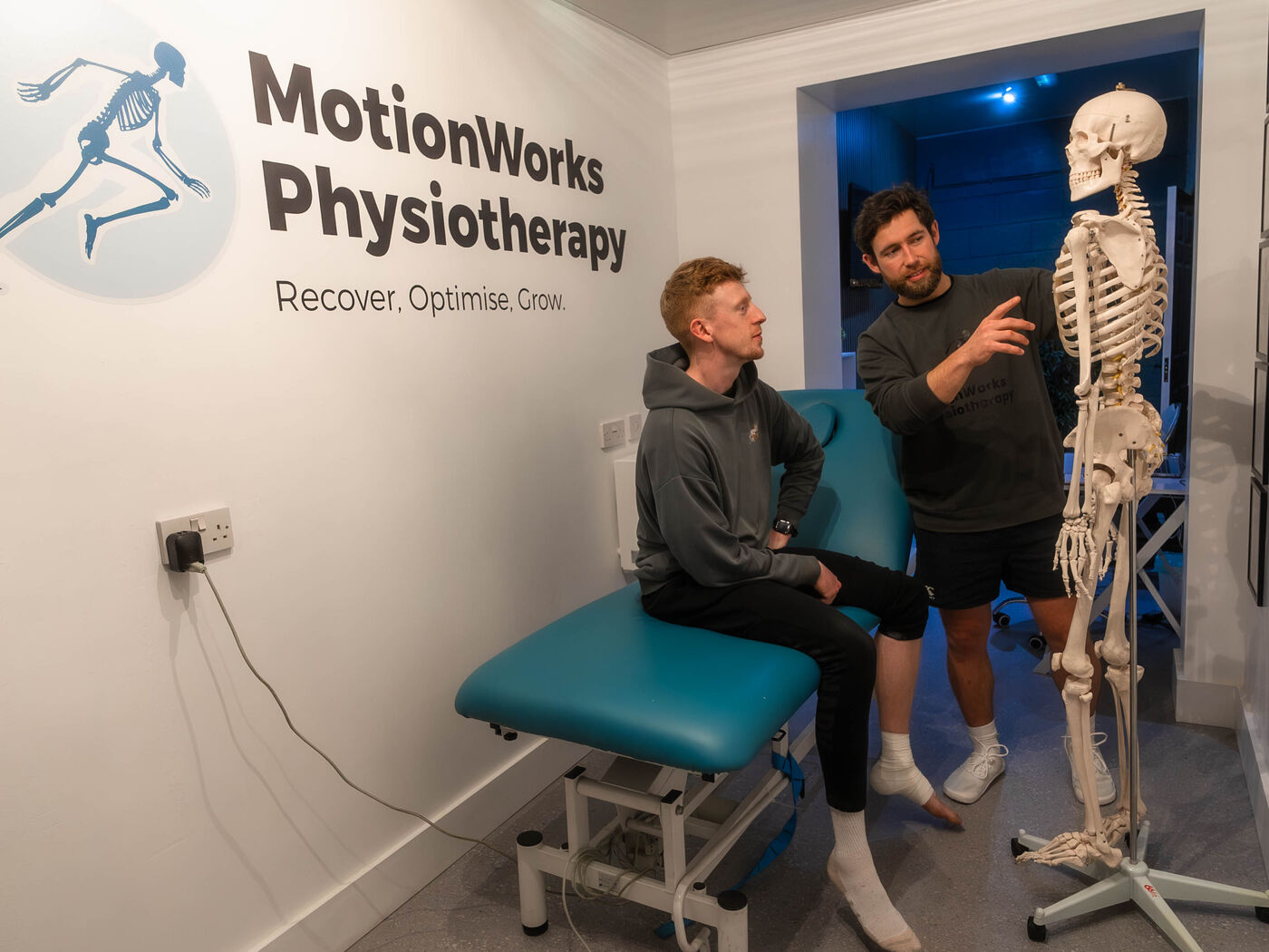 The MotionWorks treatment room, with the clinic's wall branding, a treatment plinth and a skeleton model.